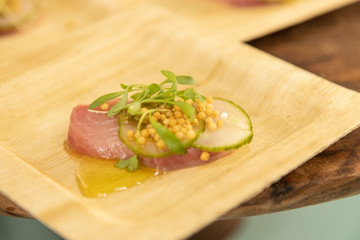 Raw tuna served paper plate with pickled cucumber and rice crackers