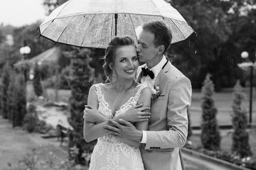 Rain at Wedding day. Happy Bride and Groom in the rainy weather are covered with a transparent umbrella