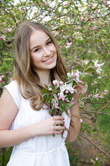 Young caucasian girl in white linen dress stay in apple garden and smile