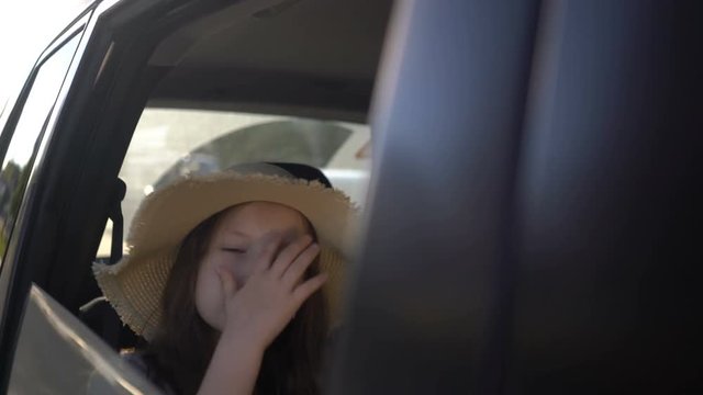 Happy beautiful girl with straw hat traveling in a car backseat. road trip concept