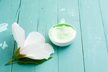 cosmetic cream and white mallow flower on blue wood table