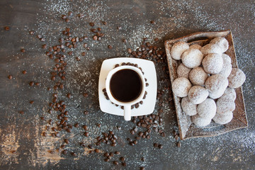 Czarna kawa w białej filiżance obok tacy z mini pączkami posypanymi cukrem pudrem © Monika