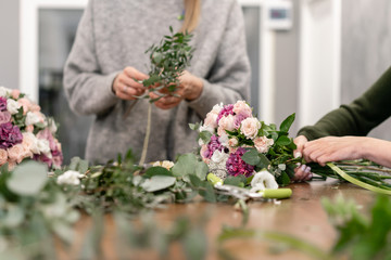 Close-up flowers in hand. Florist workplace. Woman arranging a bouquet with roses, carnation and...
