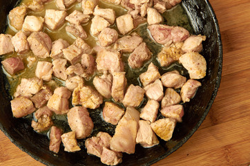 Meat, cooked on pan, cut into cubes on a wooden Board