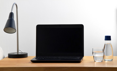 Home office with lamp, laptop, water bottle and glass of water on wooden table