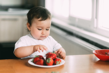 Little girl child in white t-shirt eating strawberries all smeared and dirty