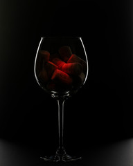 A red wine glass filled with wine corks on a black background.