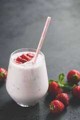 Strawberry smoothie milkshake in glass on black concrete background. Vertical orientation, toned image