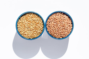 Two blue ceramic bowls of raw green and roasted buckwheat on a white background. Healthy eating concept. Top view
