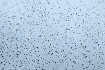 macro closeup of sparkling rain dew drops on a window glass texture pattern against sky