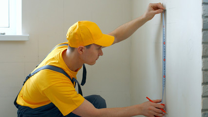 Young caucasian builder measuring wall with measuring tape. Construction worker measuring wall with...