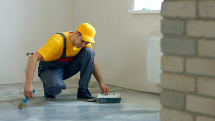 Builder renovating the house. Construction worker processing concrete floor in new apartment. Room...