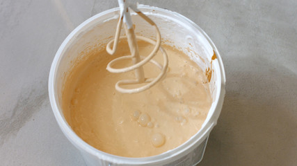 Mixing beige paint in bucket. Close up mixing primer with electric drill. DIY tools and accessory. Home renewal concept.