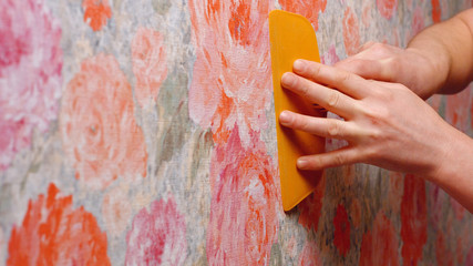 Contractor repairing apartment. Close up hand of decorator smoothing wallpaper using spatula. Home...