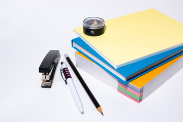 Stationery set: Multi-colored books, notebooks, textbooks, pencil sharpener, ballpoint pen, black pencil and stapler. A set of accessories for study or office work