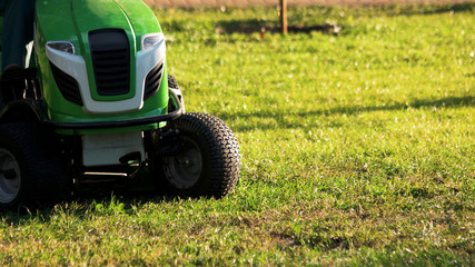Green lawn mower tractor. Lawn mower tractor outdoors on a sunny day, cropped image. © DenisProduction.com