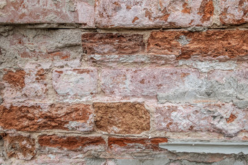 abstract background of an old brick wall with peeling plaster and the remains of pink paint close up