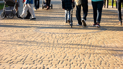 Crowd of people are walking in the park. Cubblestone pavement surface. People, vacation and leisure concept.
