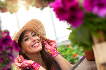 Beautiful woman florist smiling and looking flowers in garden center. Female greenhouse worker feeling happy at job.