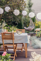 White paper lamps above garden table with chairs on stylish terrace with wooden floor and plants