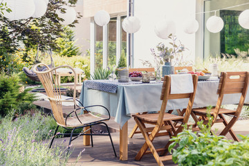 Table with wooden chairs in bright green garden of modern house, real photo