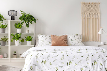 Macrame hanging on the wall in real photo of white bedroom interior with many fresh plants on rack...