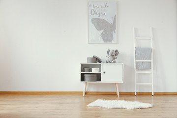 White wooden cabinet with teddy bear and round boxes in spacious baby room with butterfly poster on...