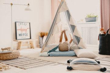 Real photo of a playroom interior with a tent, pillows and a kid having fun