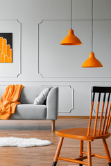 Chair in a living room interior with a wall molding, orange lamp and sofa. Real photo