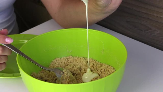 The woman adds condensed milk to the crumb of biscuits. Cooking basics for cake pops.