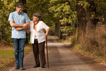 Male nurse supporting happy elderly woman with walking stick in the forest - Powered by Adobe