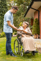 Assistant giving cup of tea to happy senior woman in the wheelchair in the garden