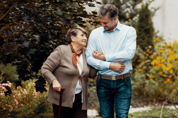 Man supporting weak senior woman with walking stick in the garden