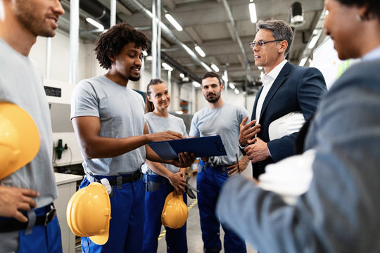 Happy African American worker showing production reports to company manager in a factory.