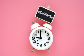 Alarm clock and word menopause on a pink background. - obrazy, fototapety, plakaty