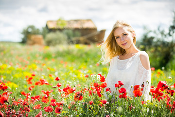 Naklejka na ściany i meble Beautiful young female in white dress in poppy field of wild flowers