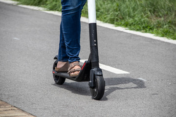 Obraz premium Woman with blue jeans and turquoise painted toenails rides an electric scooter down paved trail with grass at edge - cropped to feet and legs - selective focus