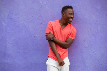 Smiling laughing African American man model posing in empty living coral color t-shirt standing against violet wall background