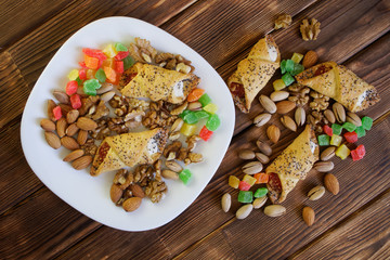 Homemade cookies with jam and poppy seeds, a mix of pistachios, almonds, walnuts and candied fruits are in a white plate on a wooden table made of pine boards