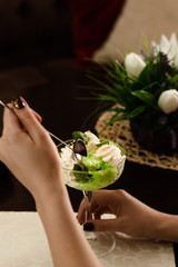 Girl eating Green and white ice cream balls scoops with syrup in a bowl on a wooden table