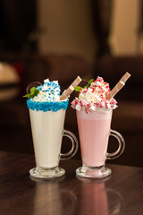 Two decorated milkshakes pink and blue on a wooden table