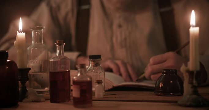 A man skilled in apothecary with his bottled medicinal concoctions on the table where he is sitting writing in a journal.