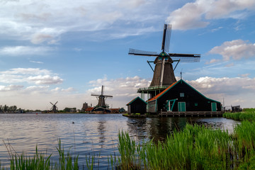 Fototapeta na wymiar Holland countryside landscape with traditional dutch windmills in sunny day in the historic village of Zaanse Schans, a neighbourhood of Zaandam, near Amsterdam in the Netherlands.