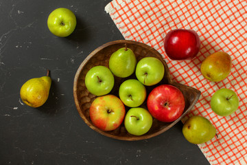 Tabletop photo - apples and pears in wooden carved bowl on black marble effect working desk with red white tablecloth