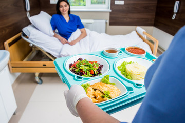 Obraz na płótnie Canvas Nurse in medical coat is holding a tray with breakfast for the young female patient.