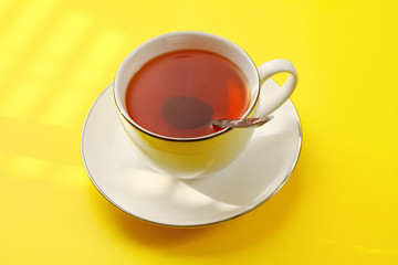 Sun shines over cup of hot tea with silver spoon on yellow board.