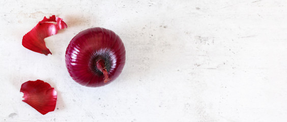 Single red onion, some skin peeled, on stone board, top down view, wide banner with copy space for text right