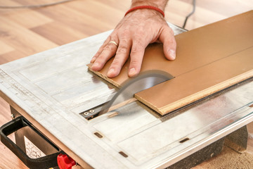 Fototapeta na wymiar Man cutting laminate floor boards on circular saw, detail on hands holding wooden panel