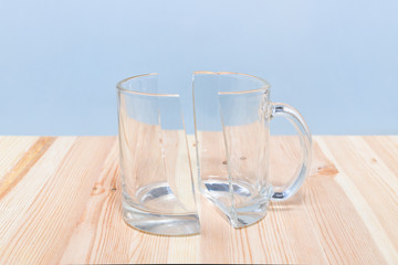 Broken glass cup on wooden table, two halves