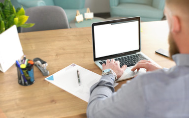 Anonymous man blurred from back working on his laptop in office, notepad, markers and calendar at desk, view from behind, detail on hands over keyboard